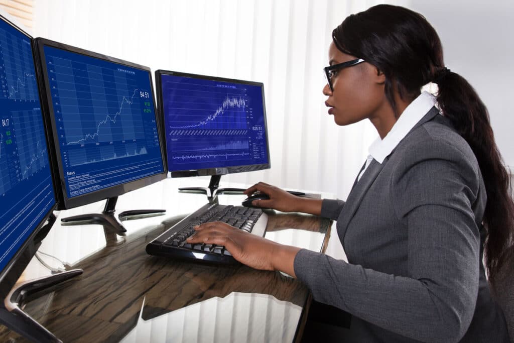 Young professional woman studying stock market graphs on three computer screens