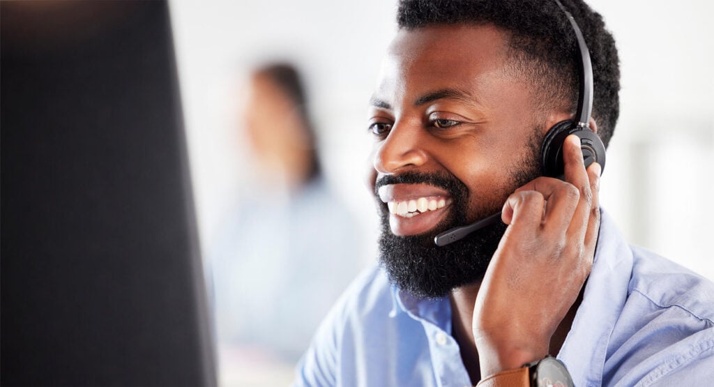 A close-up of a customer support agent smiling while using advanced customer care technology. The image emphasizes the use of conversational IVR, customer care analytics, and customer care automation to enhance customer experiences. Harte Hanks implements innovative customer care chatbots and customer care management systems for seamless, scalable support.