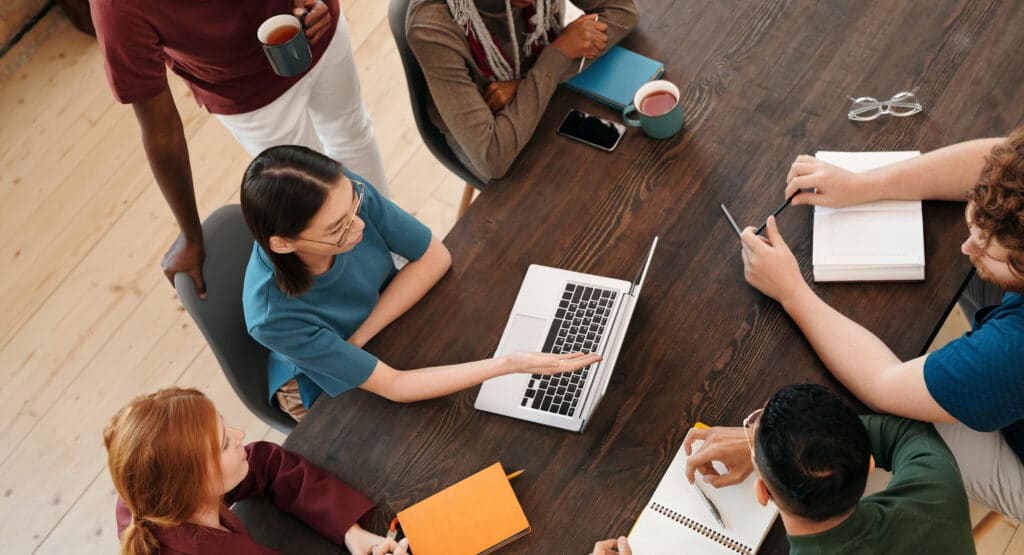 A diverse team of professionals collaborating around a laptop, showcasing effective teamwork and innovative marketing strategies in a dynamic workspace. This image represents Harte Hanks' commitment to providing exceptional marketing strategy services, emphasizing client relationship management and customer engagement strategies.