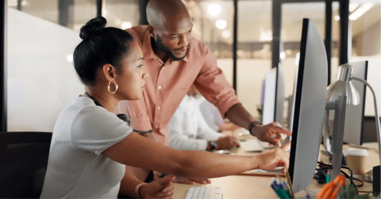 A business professional mentors a colleague in a modern office setting, discussing talent development, hybrid work models, and the future of work. The collaboration reflects evolving workforce trends, employee engagement strategies, and the impact of the Great Resignation on workplace dynamics.